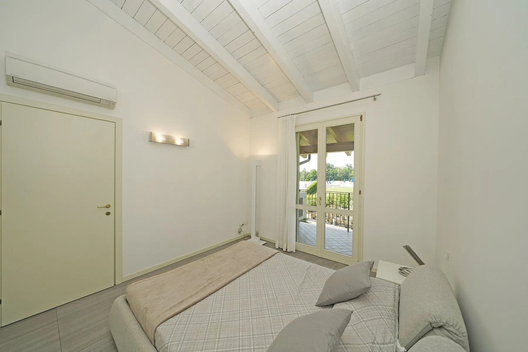 Un dormitorio luminoso con una cama junto a puertas de vidrio que dan a un balcón.