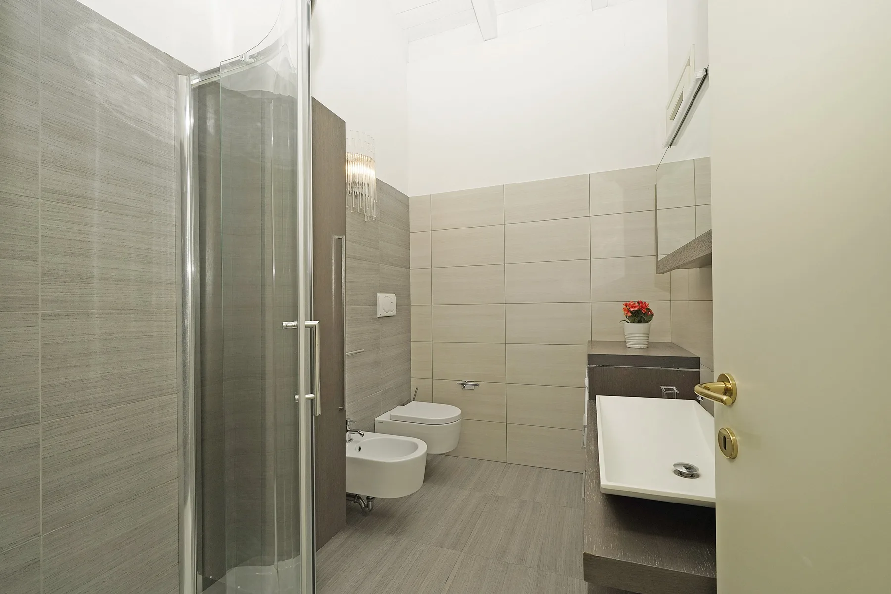 Un baño alicatado con ducha de vidrio y lavabo suspendido.