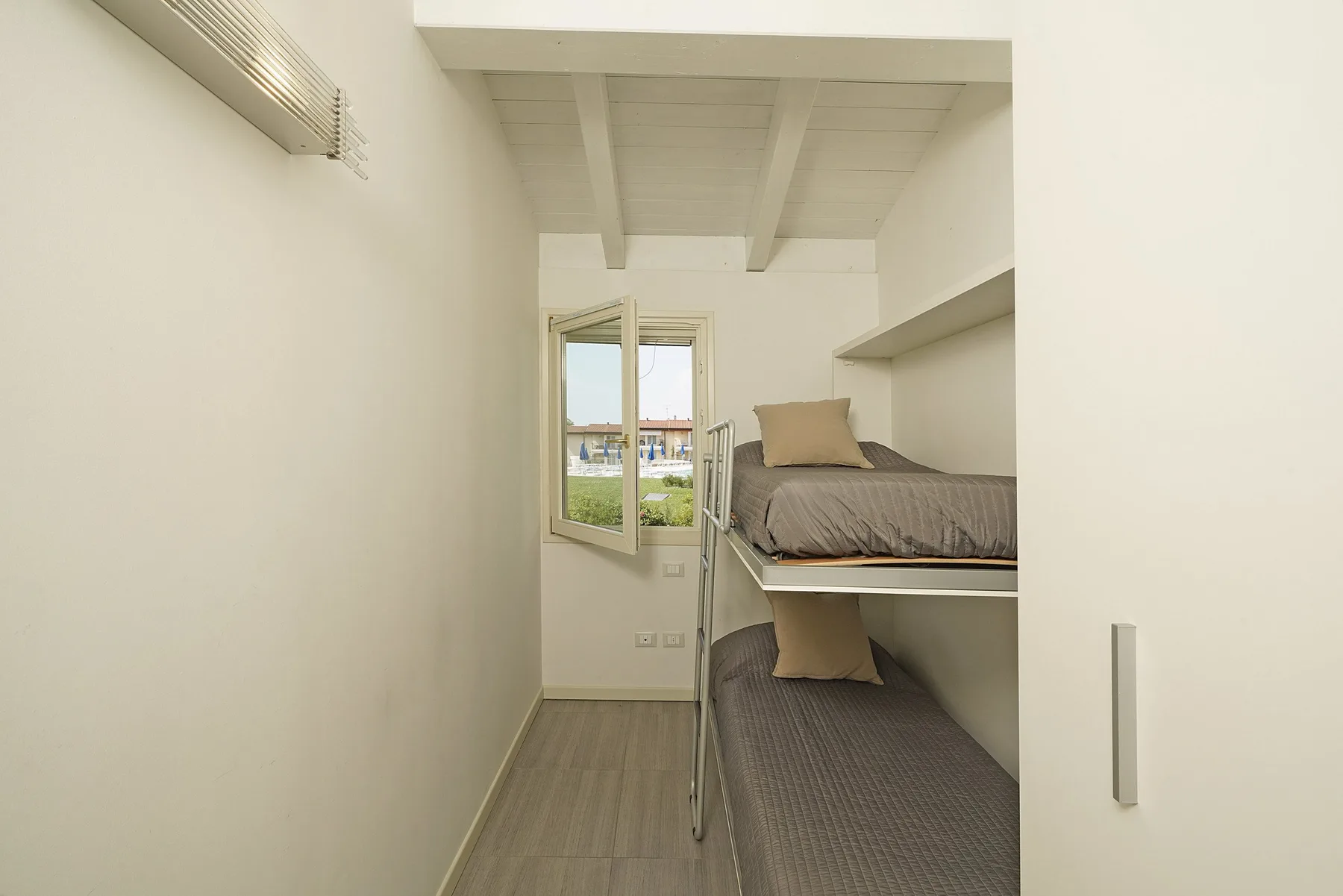 Un dormitorio estrecho con dos camas apiladas y una ventana abierta.