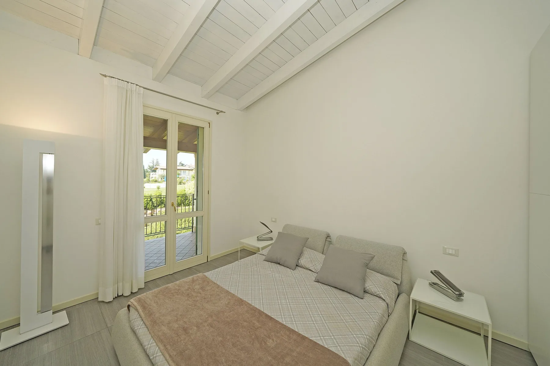 Un dormitorio luminoso con una cama, una mesita y puertas de vidrio que dan a un balcón.