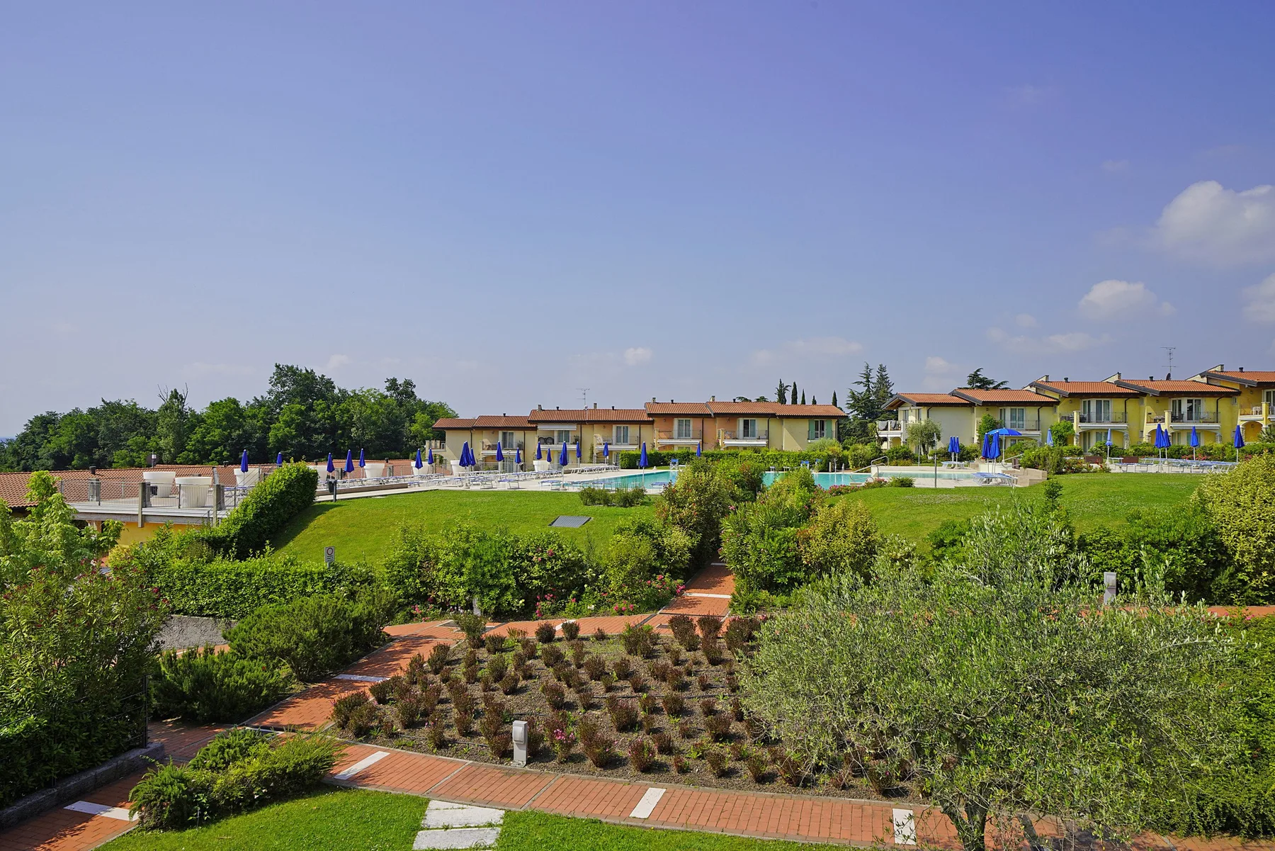 Un jardín ajardinado con senderos de ladrillo y edificios bajos al fondo.