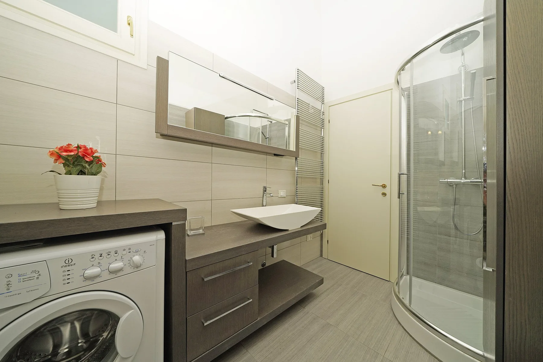 Un baño con lavabo, lavadora y ducha de cristal.