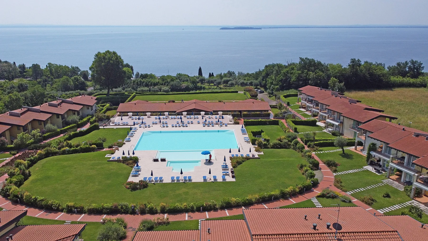 Vista aérea de un complejo con piscina, jardines y el mar al fondo.