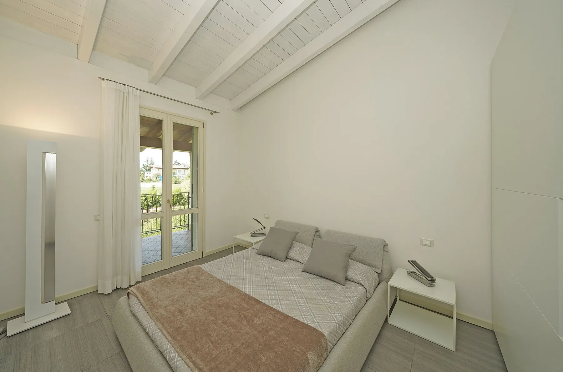 Un dormitorio luminoso con una cama junto a puertas de vidrio que dan a un balcón.
