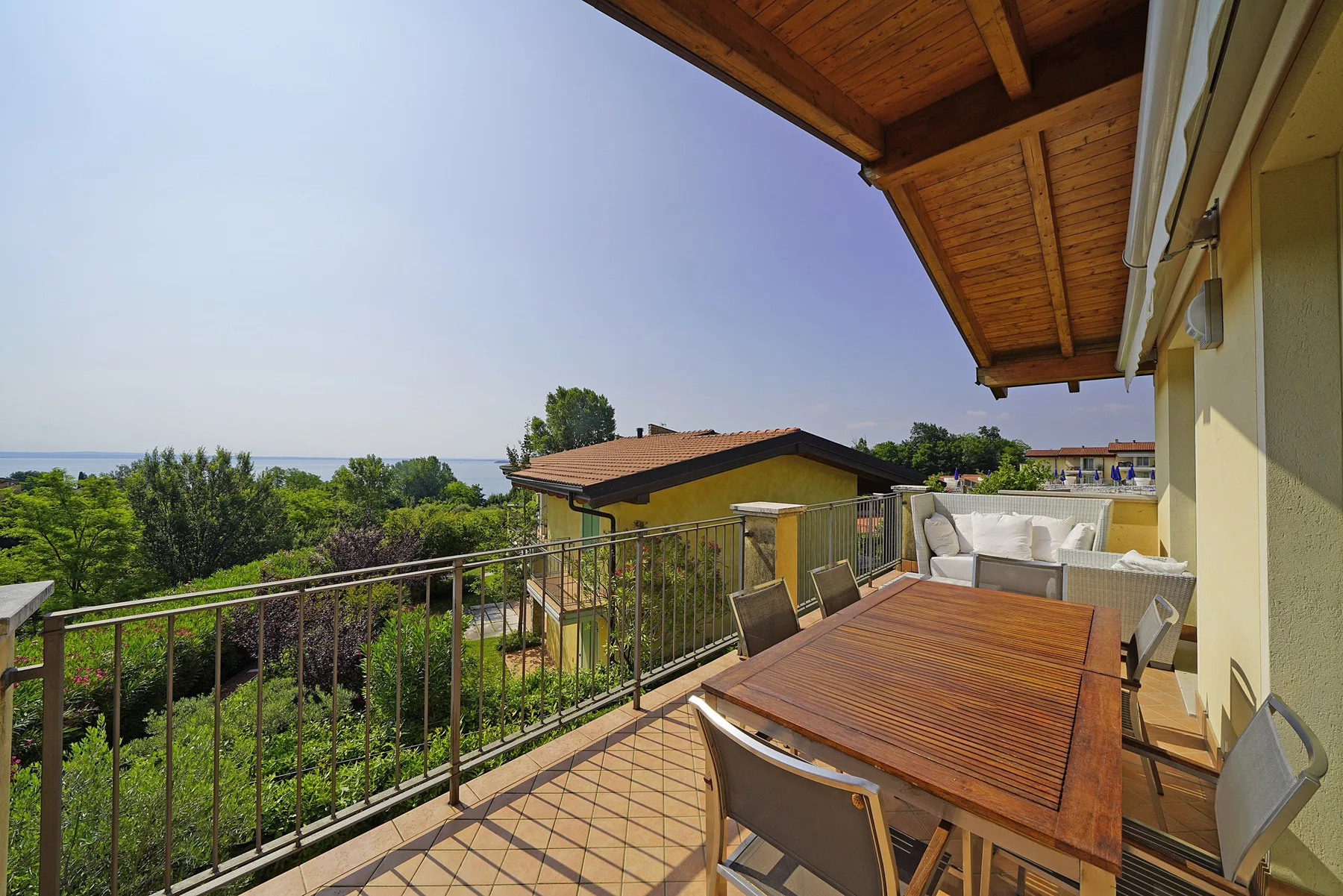 Una terraza con una mesa de comedor de madera da a la vegetación y al mar.