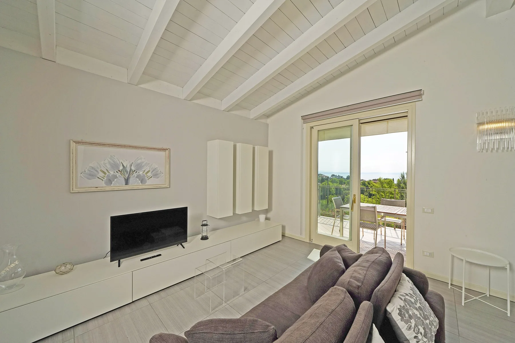 Una sala luminosa con asientos, un televisor y puertas de vidrio que dan a un patio.