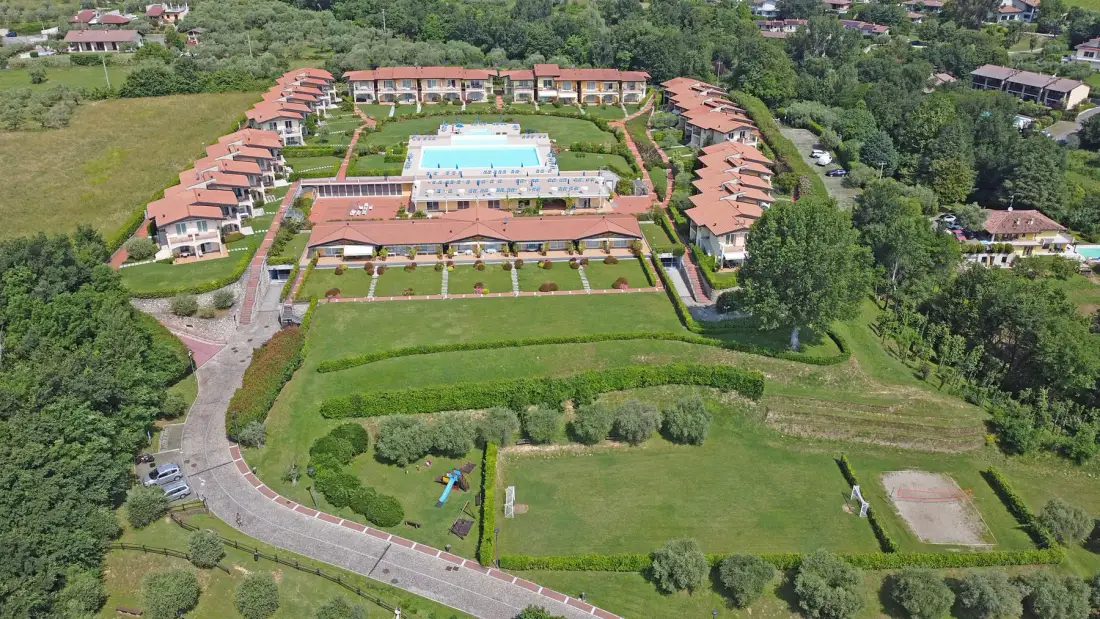Una vista aérea muestra un complejo ajardinado con una piscina central y edificios alrededor.