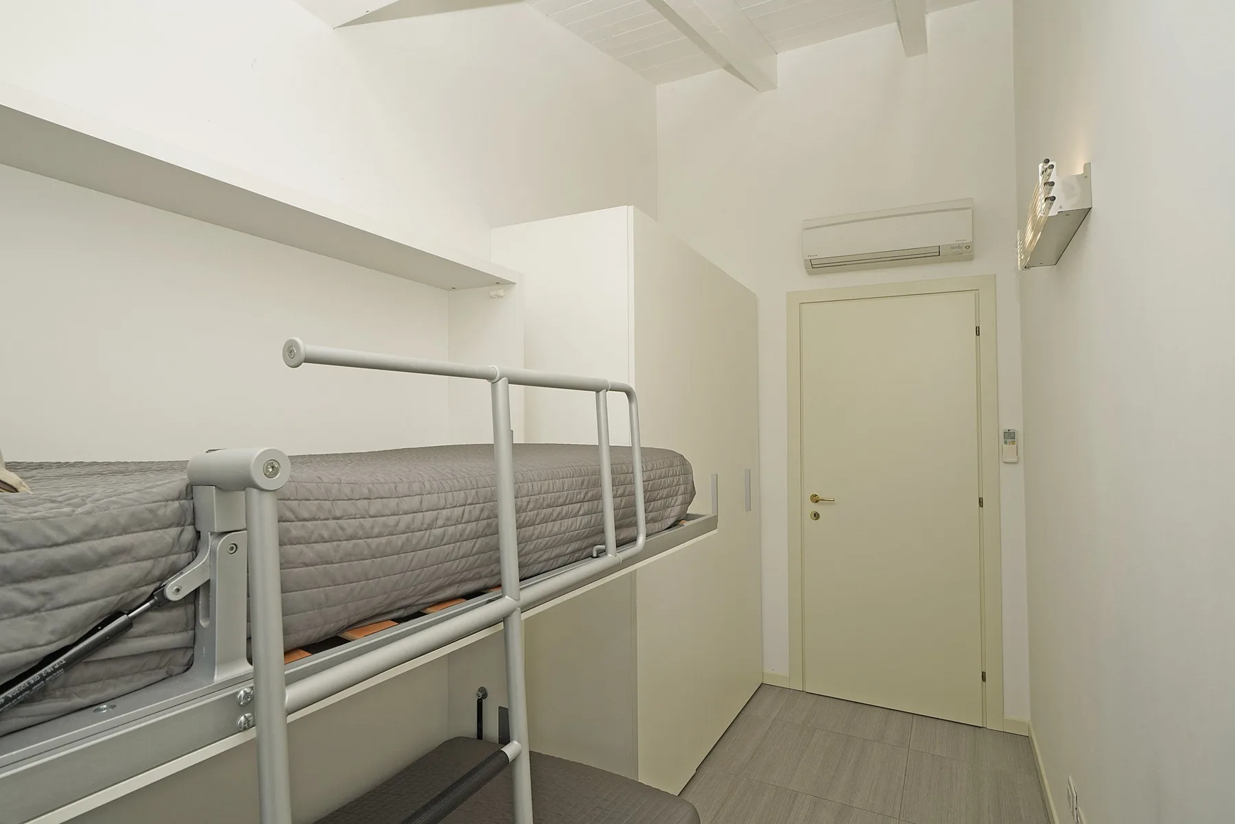 Una zona compacta para dormir, con una cama elevada junto a una puerta cerrada.