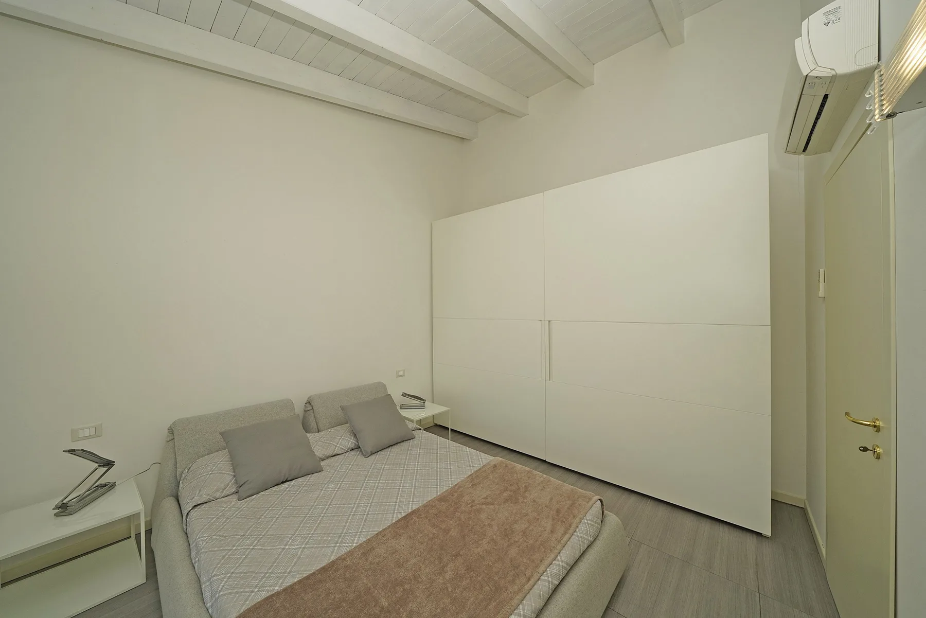Un dormitorio con una cama, un gran armario blanco y un aire acondicionado.