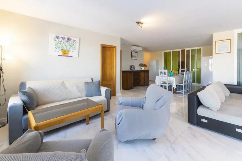 A bright living room with seating, a coffee table, and a dining area in the background.