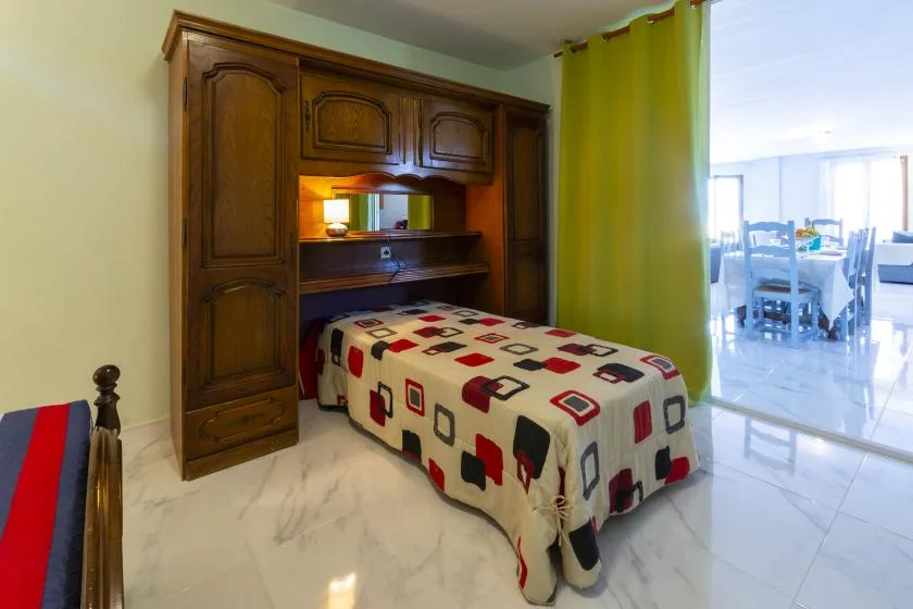 A bedroom with a bed beneath a built-in wooden cabinet and a green curtain.
