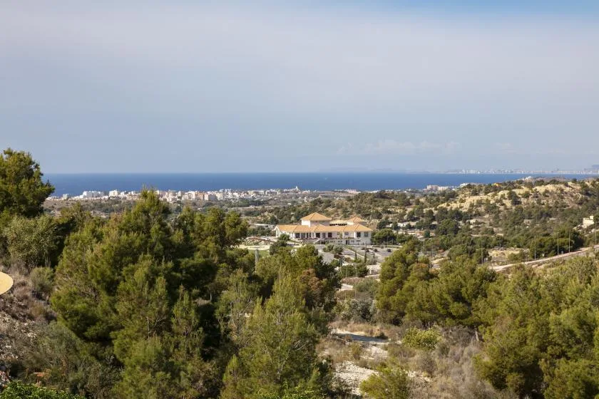 A coastal landscape with scattered buildings, trees, and the sea in the distance.