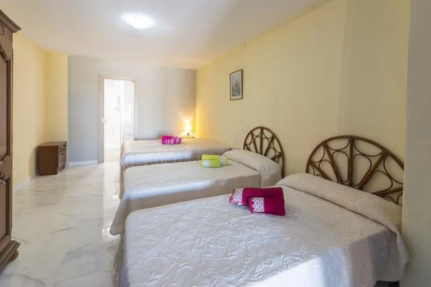 A bedroom with several beds arranged in a row and a bright doorway.