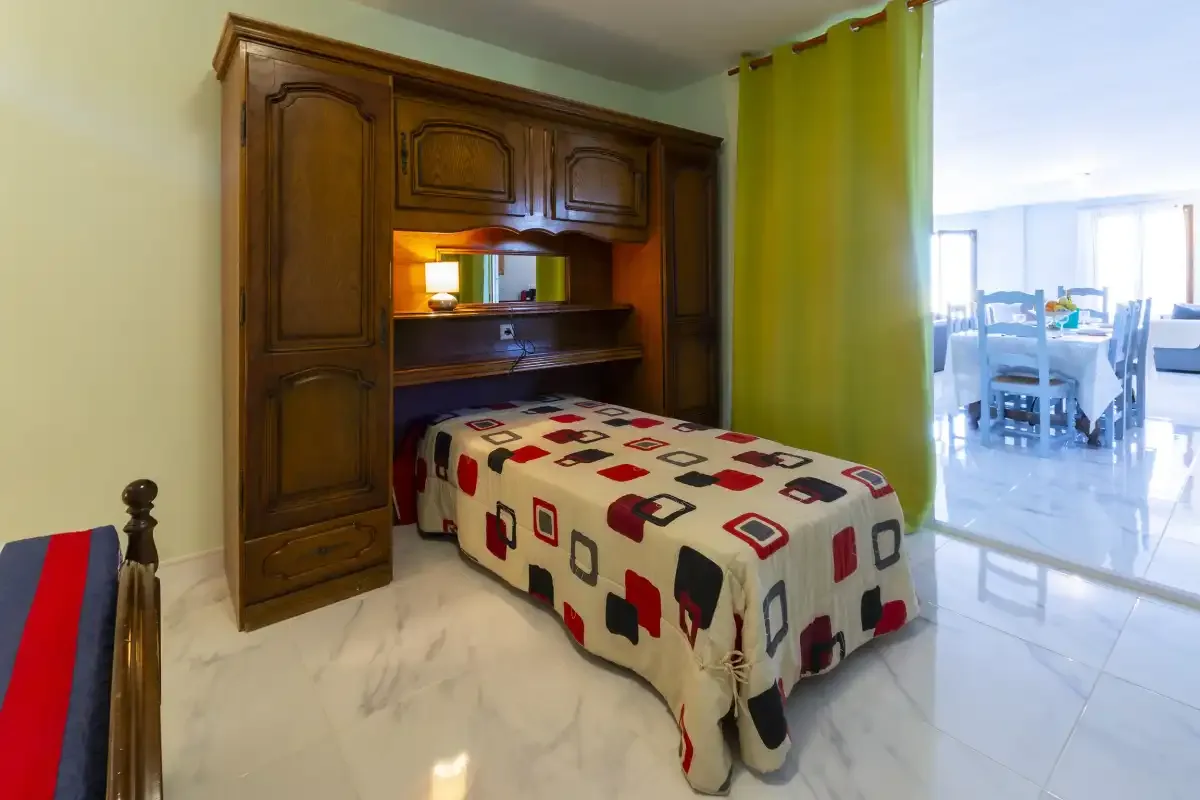 A bedroom with a bed set into a large wooden wall unit beside a green curtain.