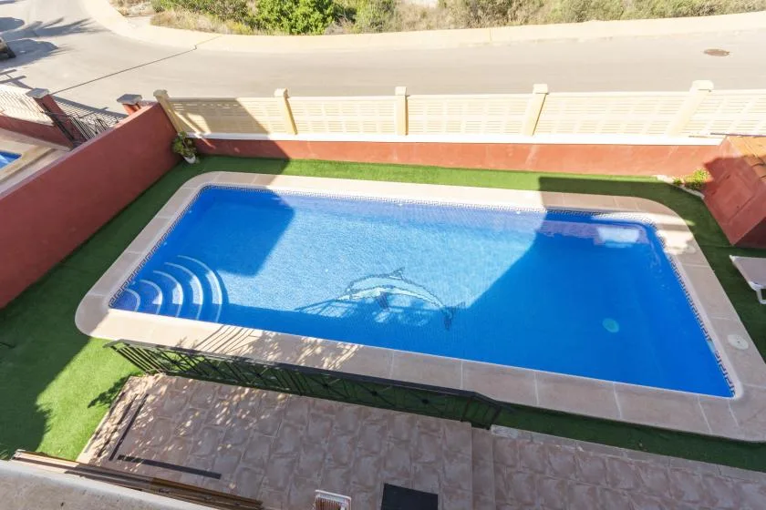 An outdoor swimming pool sits beside a paved patio and green lawn.