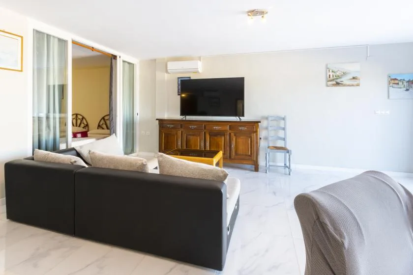 A bright living room has a dark seating area facing a television and wooden cabinet.