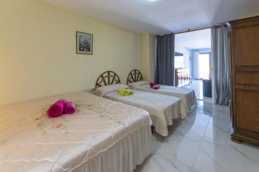 A bedroom with three beds, light bedding, and curtains beside a bright window.
