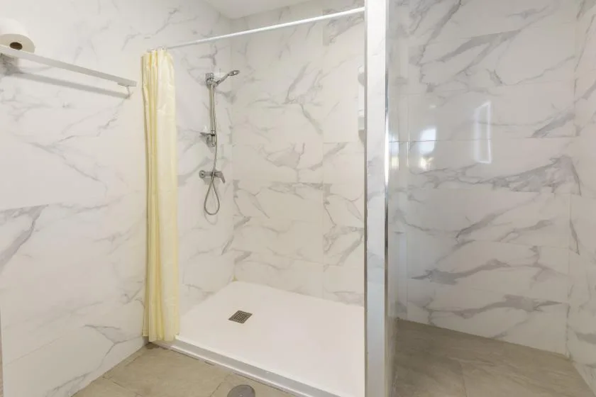 A bathroom shower area with a pale curtain and marble-patterned walls.