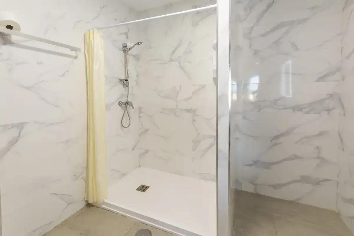 A tiled bathroom shower with a pale curtain and glass partition.