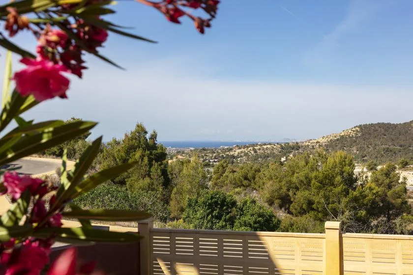 A hillside landscape with trees and distant sea, seen above a slatted fence.