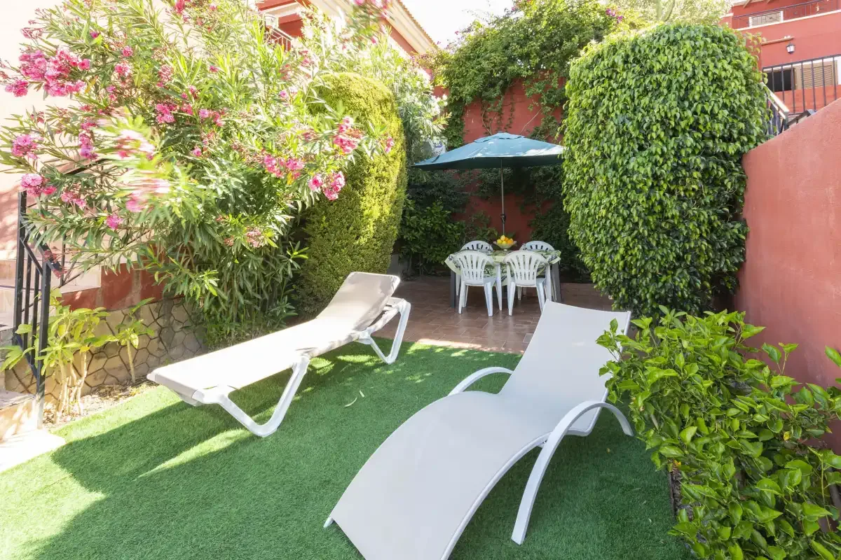 A garden patio with lounge chairs, greenery, and a shaded dining area.