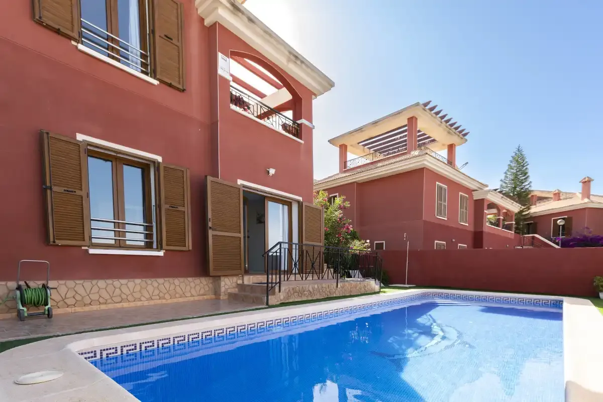 A swimming pool beside a red building with balconies and shuttered windows.