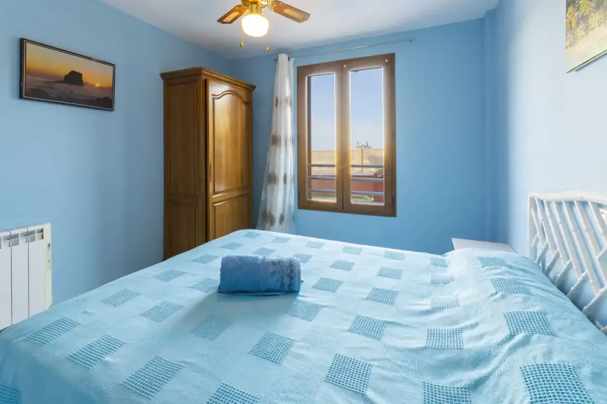 A bedroom with blue bedding, a wooden wardrobe, and a window.