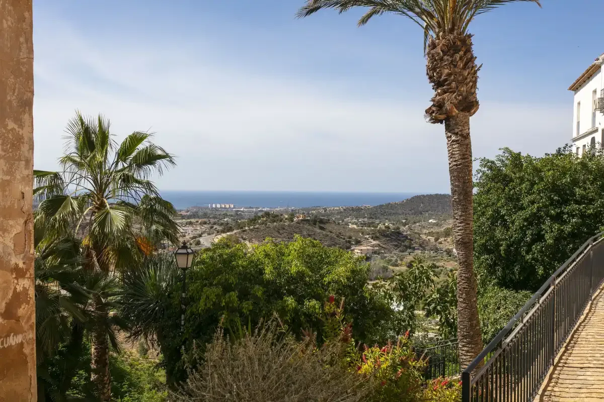 A garden terrace overlooks a coastal landscape with palm trees and the sea.