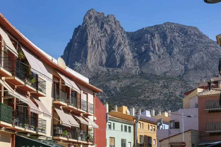 Apartment buildings line a street beneath a steep rocky mountain.