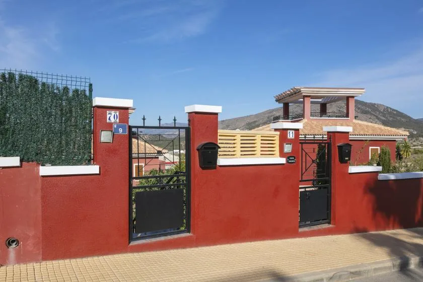 A red-walled property entrance with metal gates and a mountain in the background.