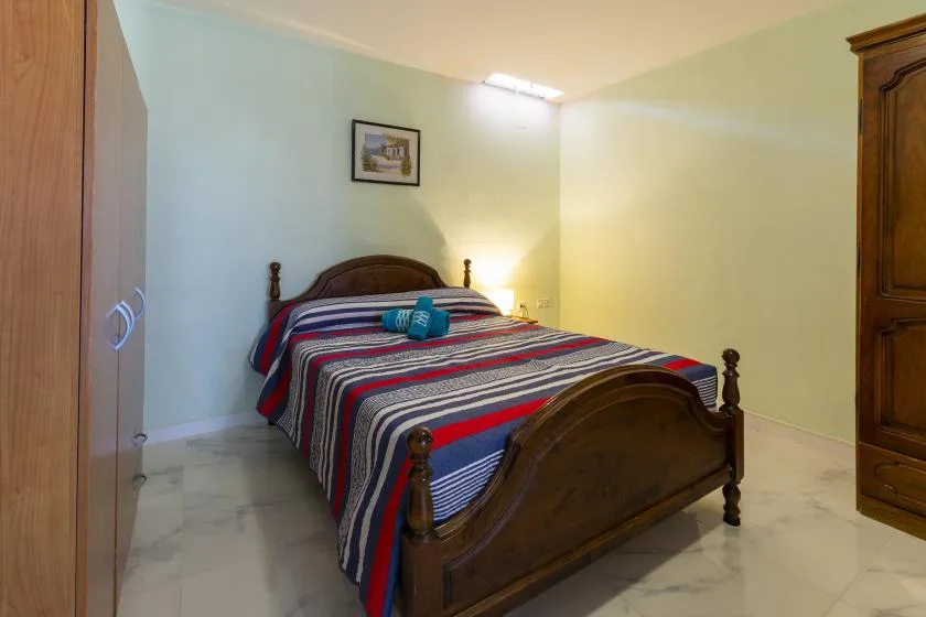 A bedroom with a wooden bed covered by a striped bedspread.