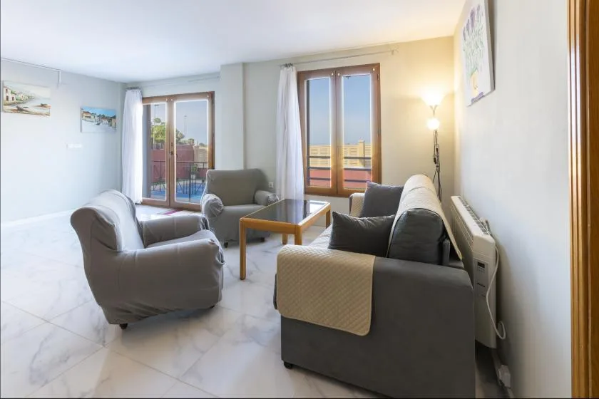 A bright living room with seating arranged around a coffee table and large windows.