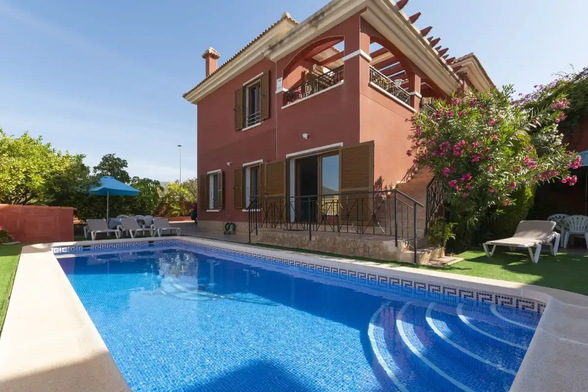 A swimming pool beside a two-story house, with loungers on the patio.