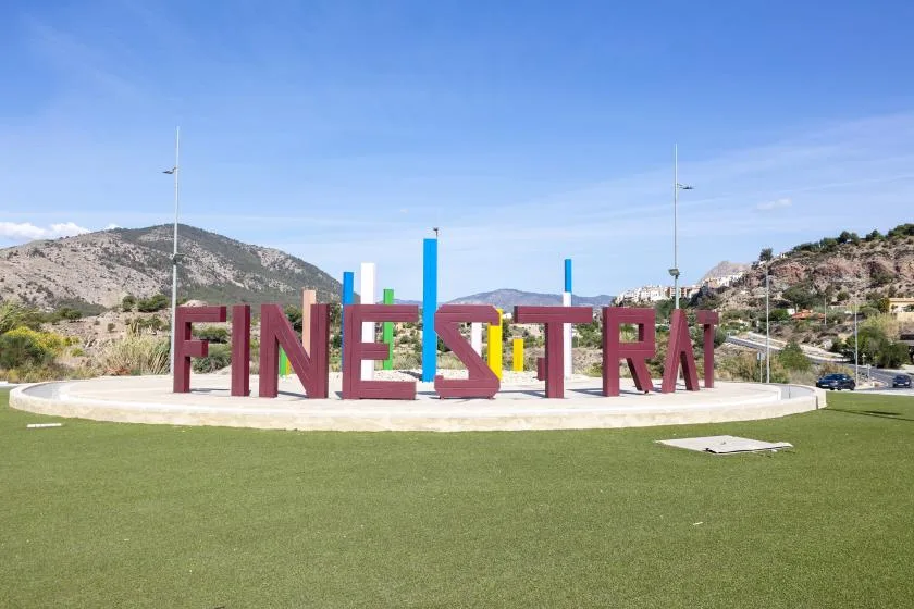 An outdoor plaza features large red letters spelling “FINESTRA” against a mountain backdrop.