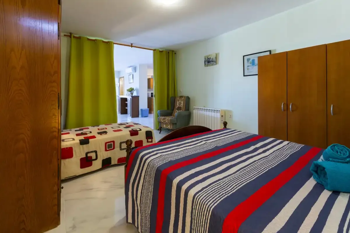 A bedroom with two beds, wardrobes, and green curtains.