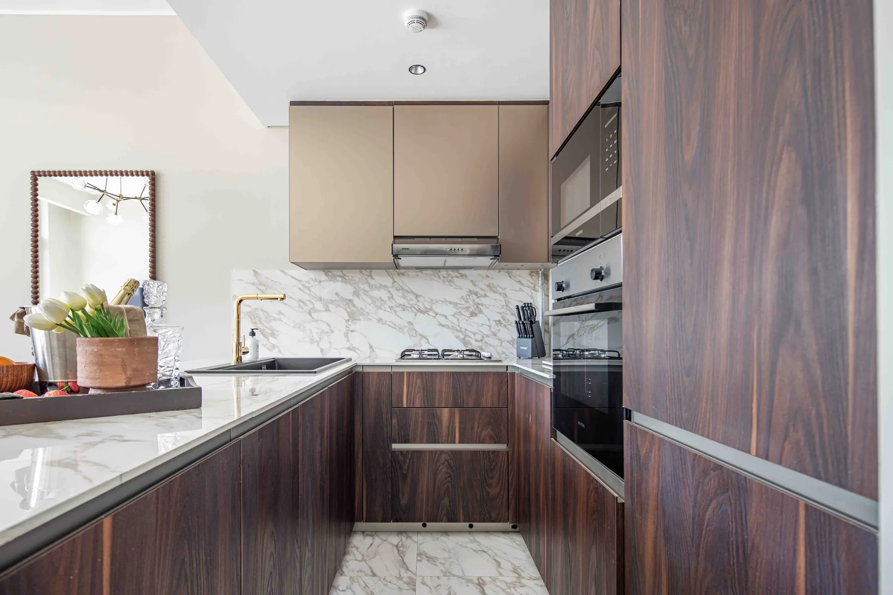 Una cocina moderna con gabinetes oscuros, una encimera con vetas marmoleadas y electrodomésticos integrados.