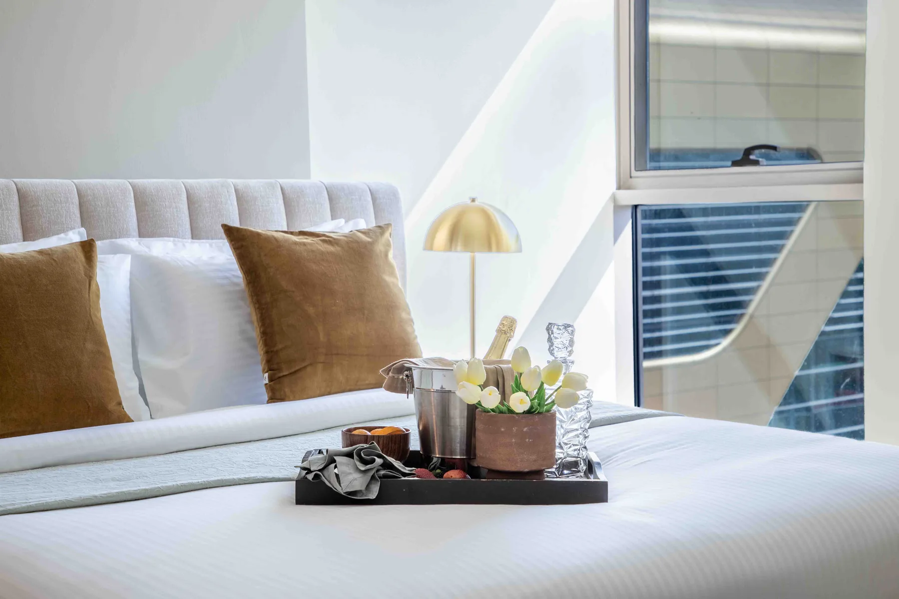 Un dormitorio luminoso con una cama tendida y objetos decorativos sobre una bandeja.