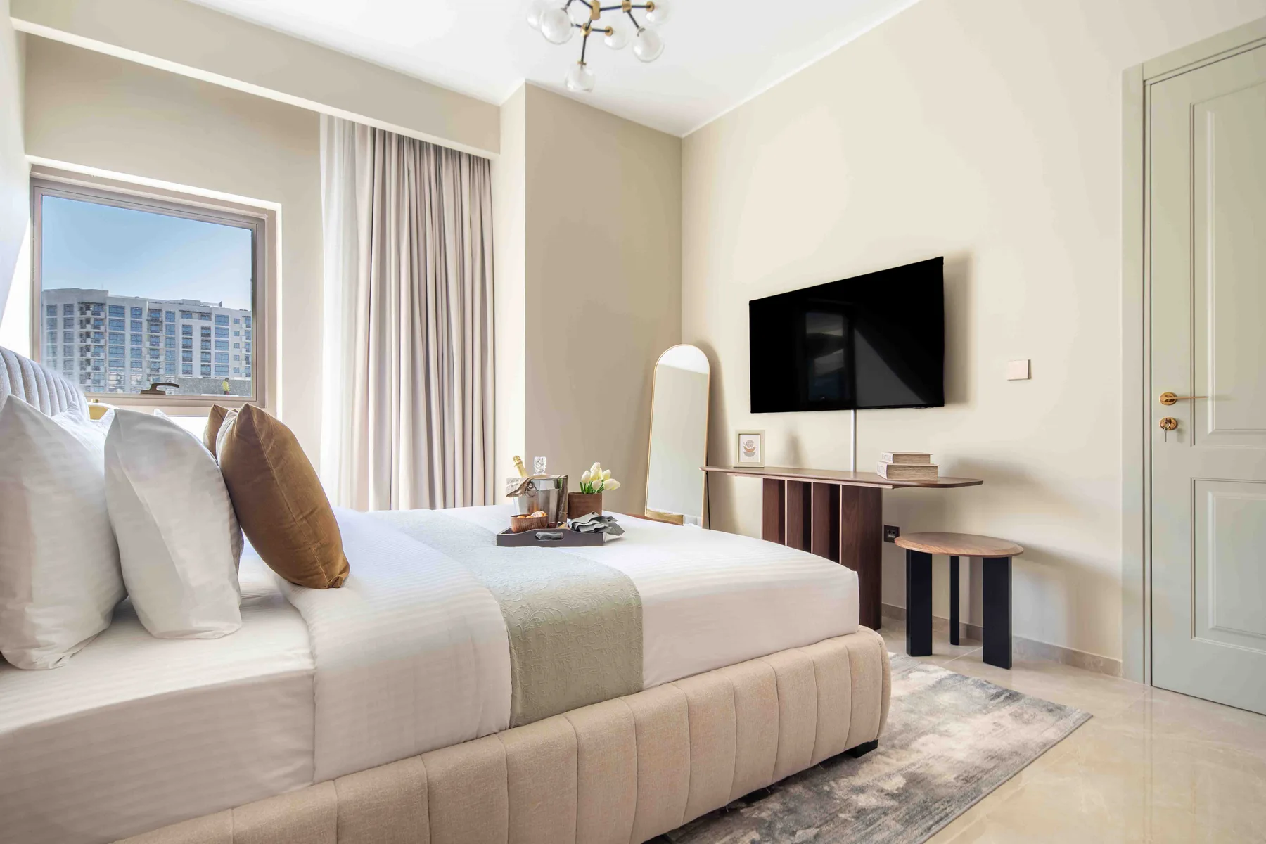 Un dormitorio luminoso con una cama bien tendida y un televisor montado en la pared.