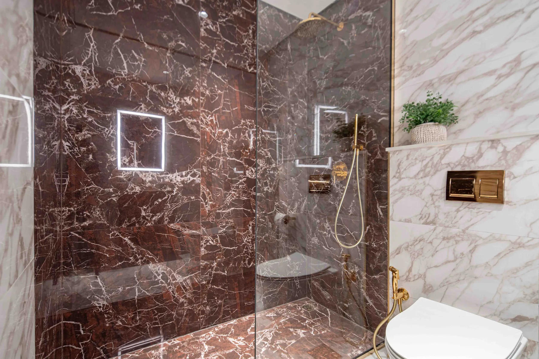 Un baño revestido de mármol con ducha de cristal, grifería dorada e inodoro.