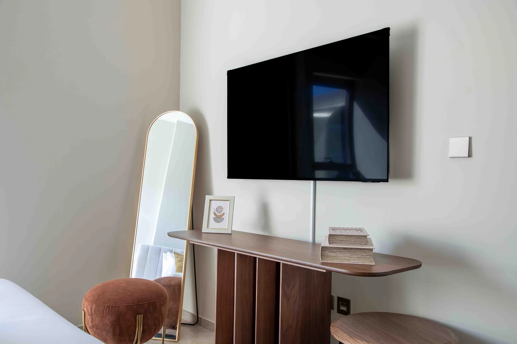 Un rincón de dormitorio tiene un televisor montado en la pared sobre un escritorio de madera.