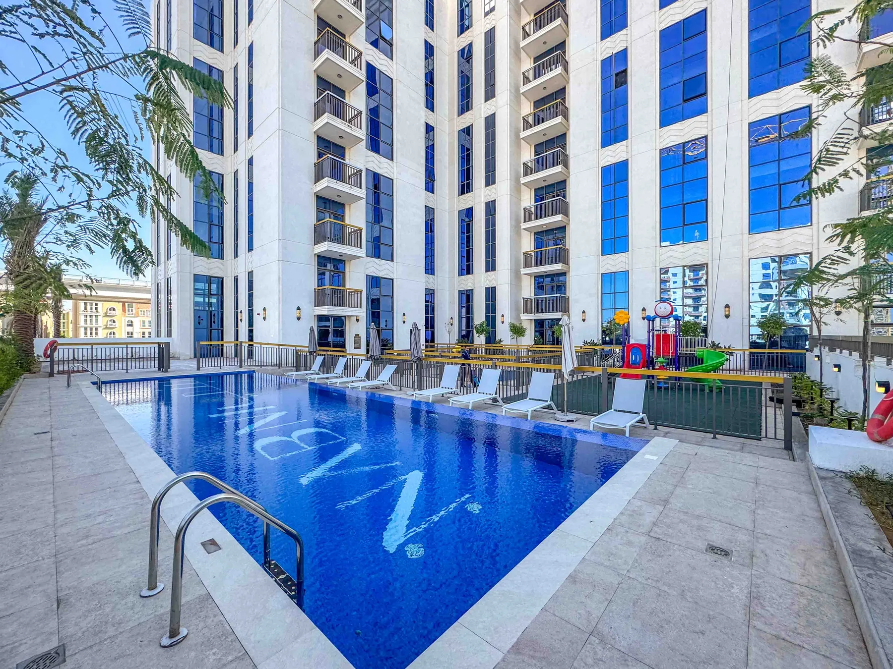 Una piscina al aire libre está junto a un edificio moderno alto.