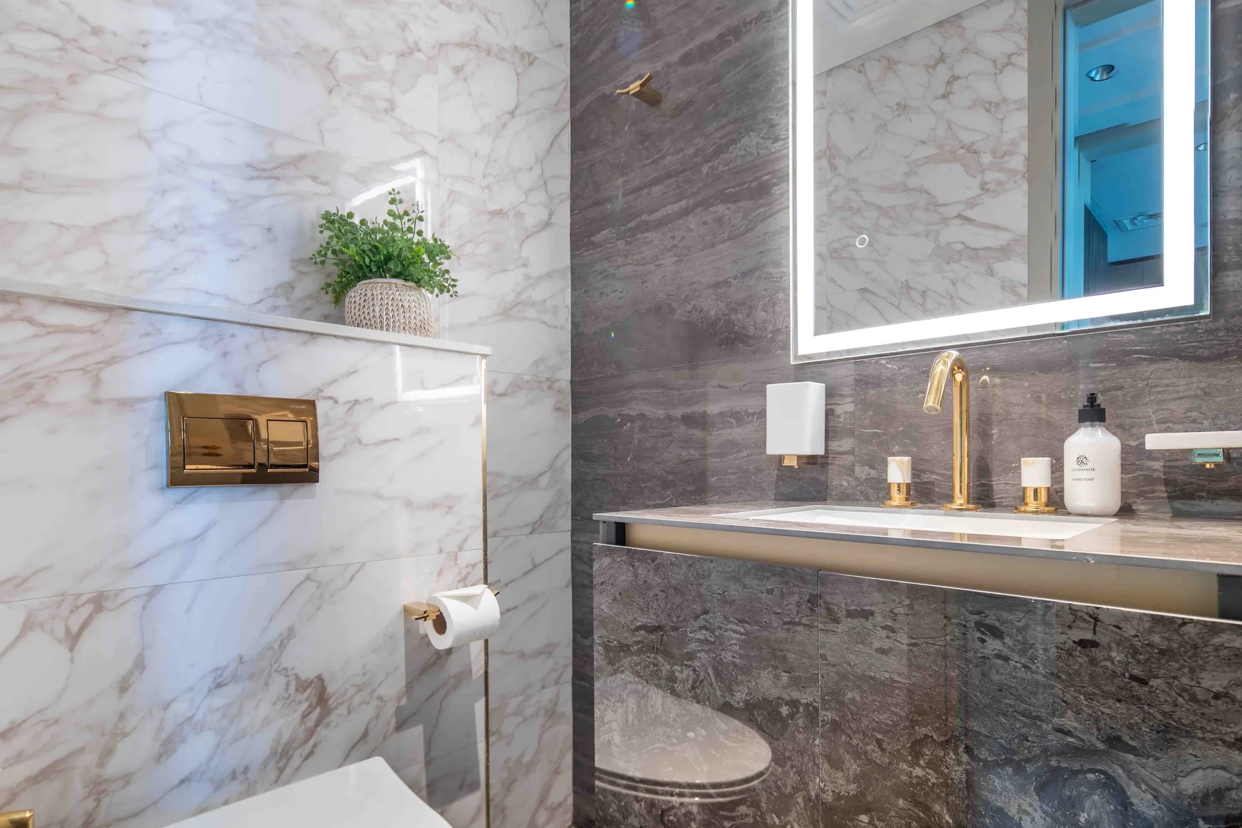 Un lavabo de baño con acabado marmoleado, grifo dorado y un espejo grande.