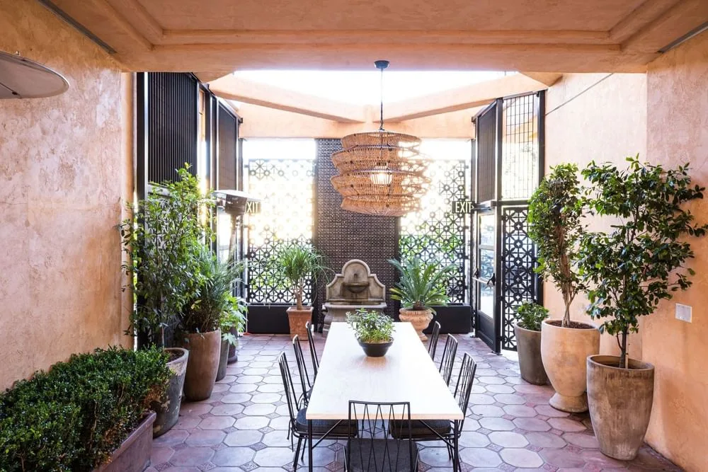 Zona de comedor al aire libre con mesa, fuente y plantas en macetas