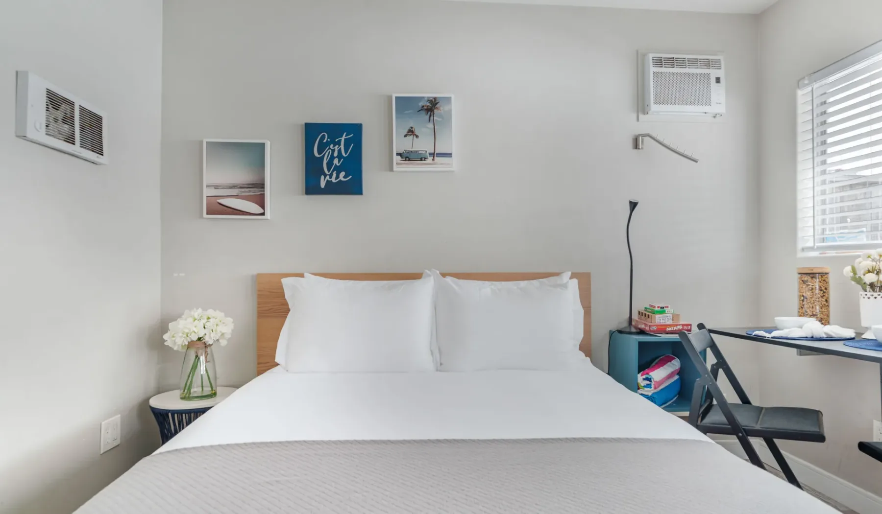 Un dormitorio luminoso con una cama tendida y cuadros en la pared.