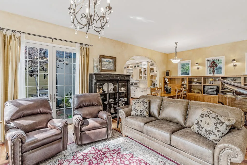 A living room with cushioned seating, a chandelier, and bookshelves along the back wall.