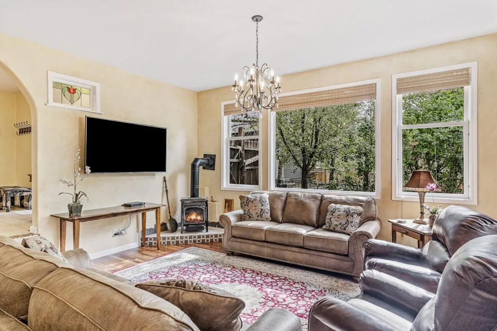 A bright living room with seating, a fireplace, and large windows overlooking greenery.