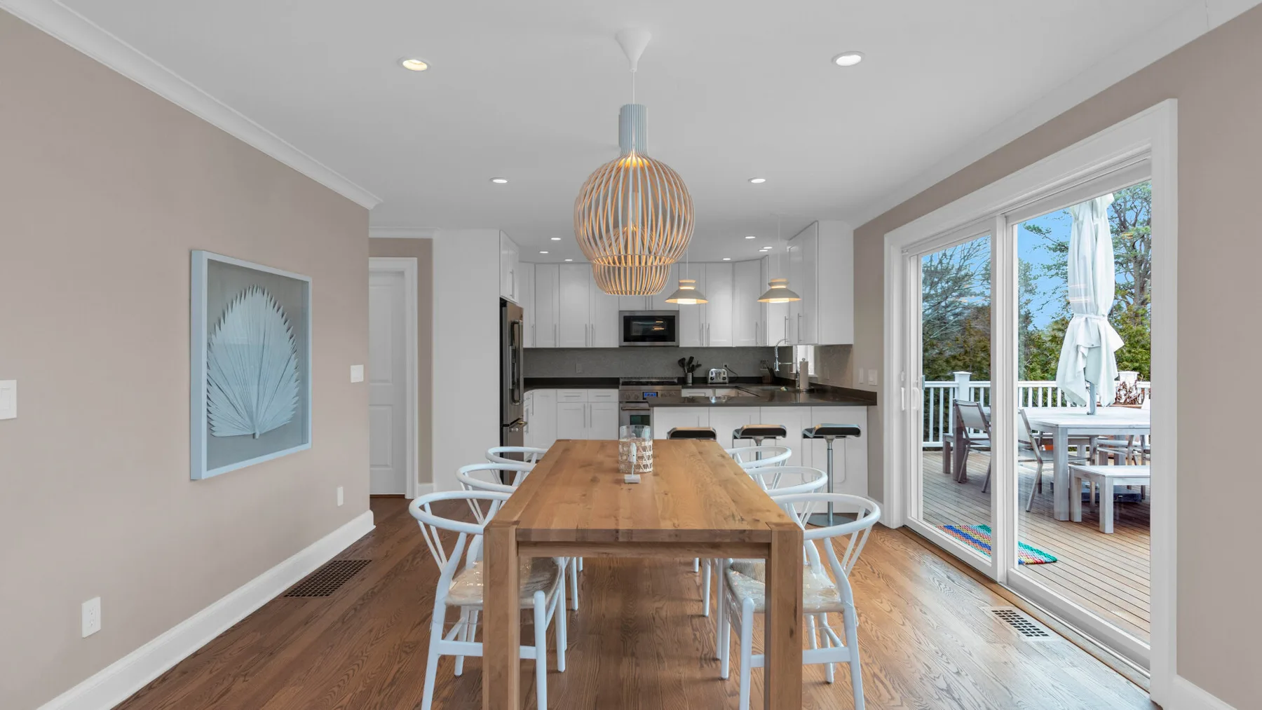 A bright dining area with a long wooden table and glass doors opening onto a deck.