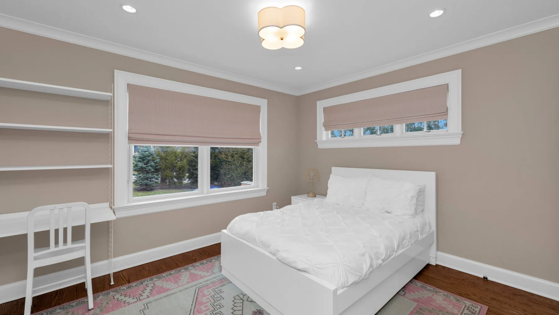 A bedroom with a bed, a desk, and windows with blinds.