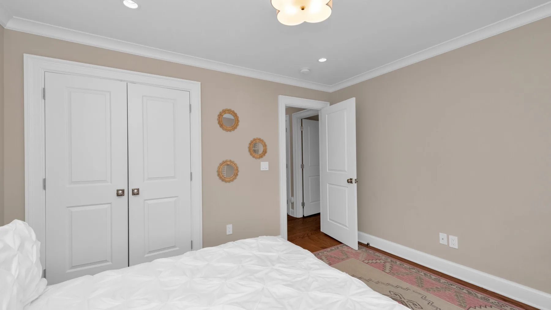 A bedroom with a white bed, closet doors, and an open doorway.