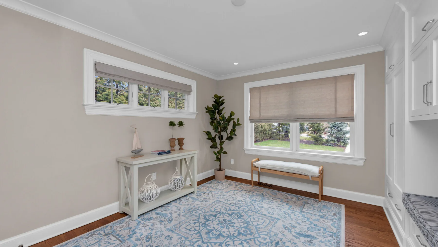 A bright living area has a patterned rug, a console, and windows overlooking greenery.